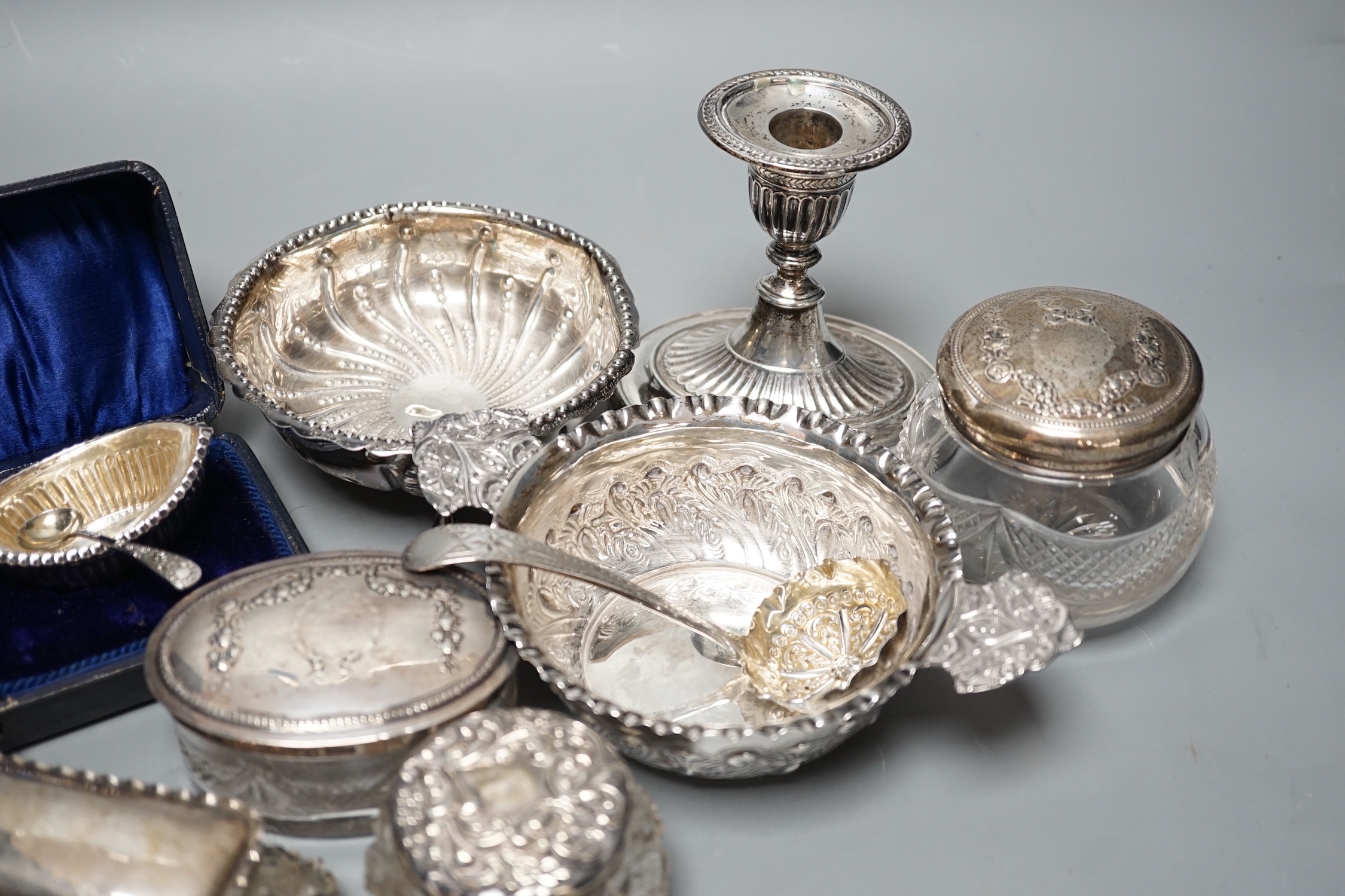 A Victorian repousse silver two handed bowl, one other silver bowl, a silver sifter spoon, four silver mounted glass toilet jars, a silver dwarf candlestick and a cased pair of silver salts.